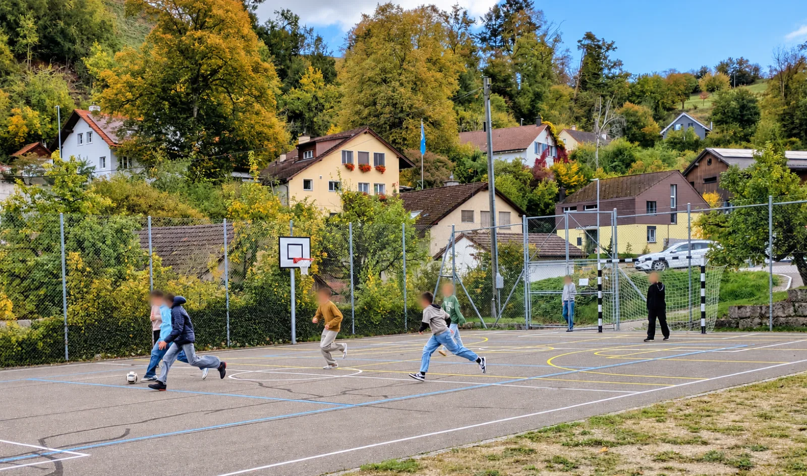 Jugendliche spielen Fussball auf einem Sportplatz.