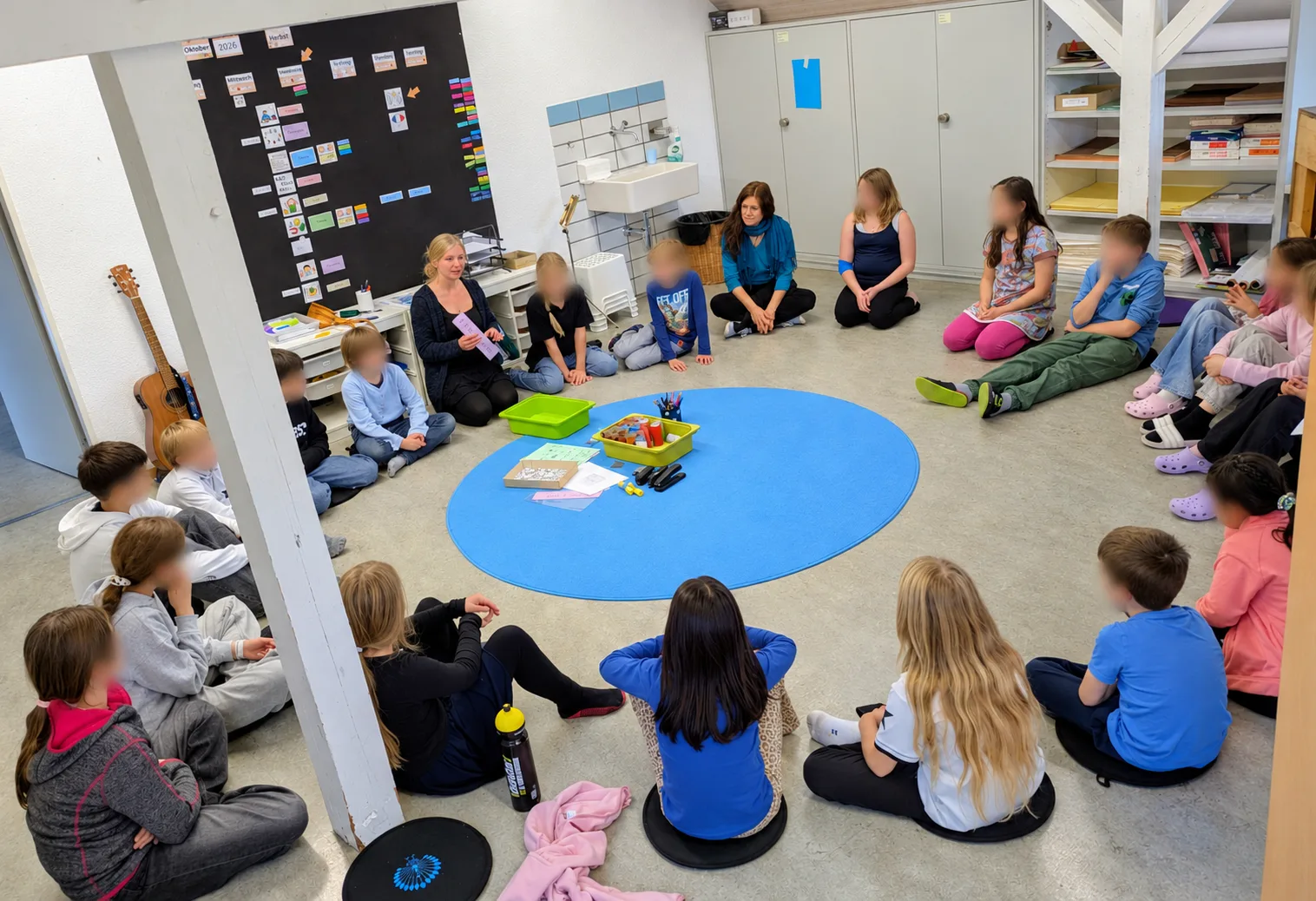Kinder sitzen in einem Kreis zusammen, die Lehrerin erklärt etwas.