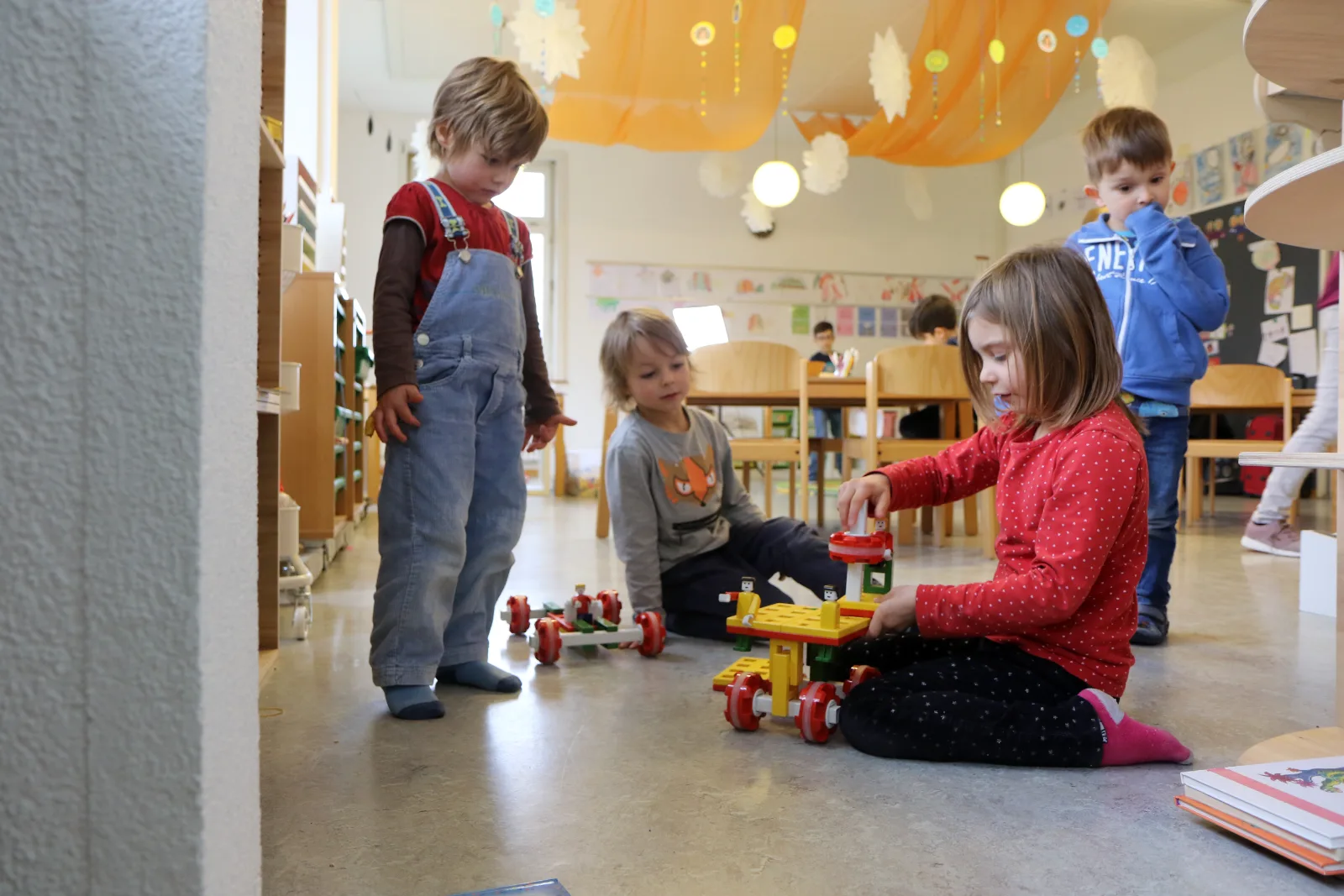 Drei Kinder lachen aus einer grossen Kiste in der Turnhalle